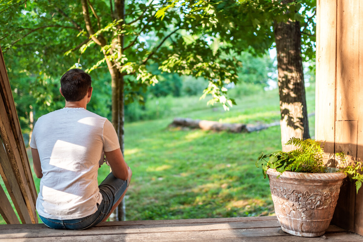 Homeowner sitting on porch looking over backyard lawn after storms while planning yard drainage improvements